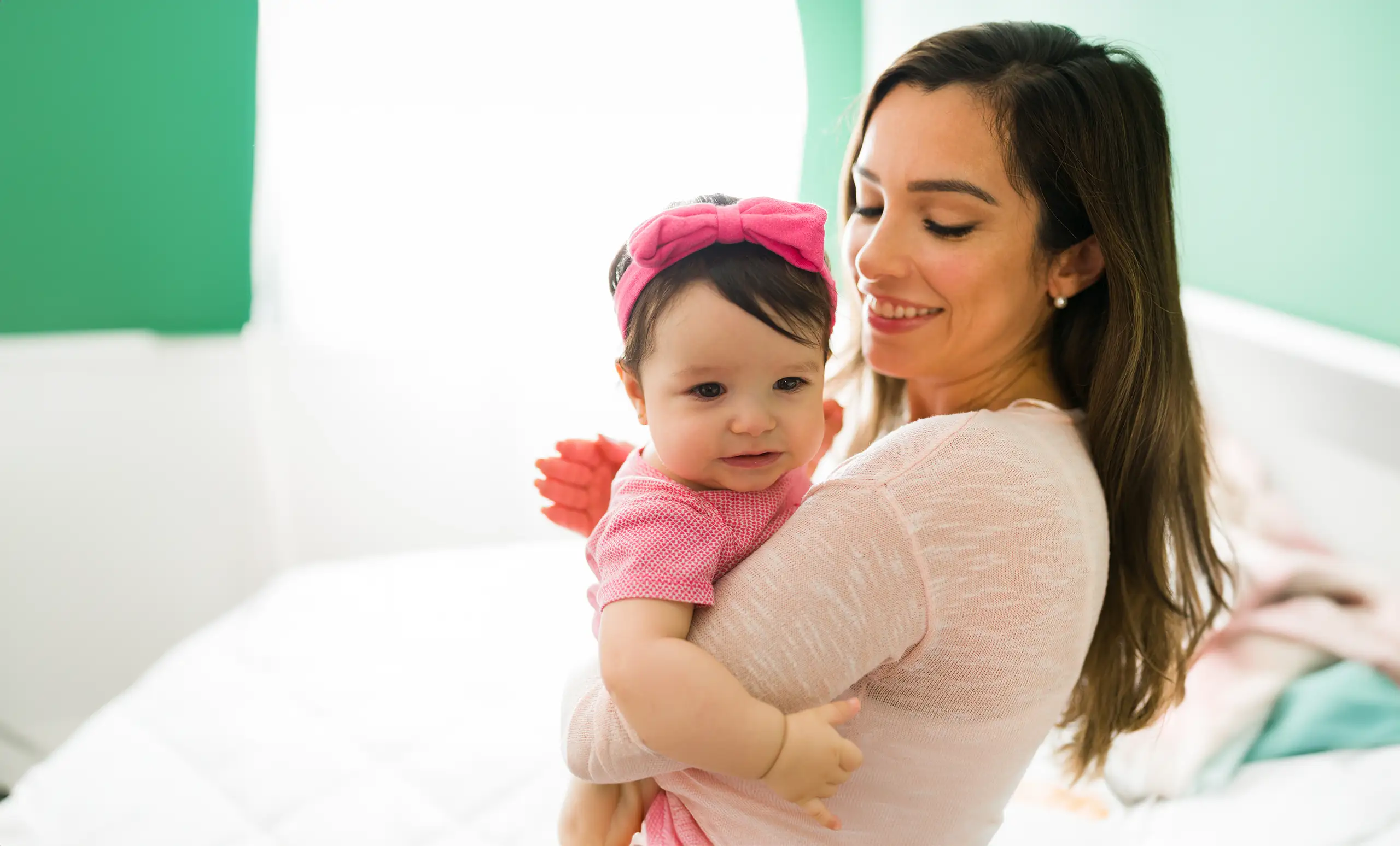 Young mother burping a baby girl wearing a pink onesie.