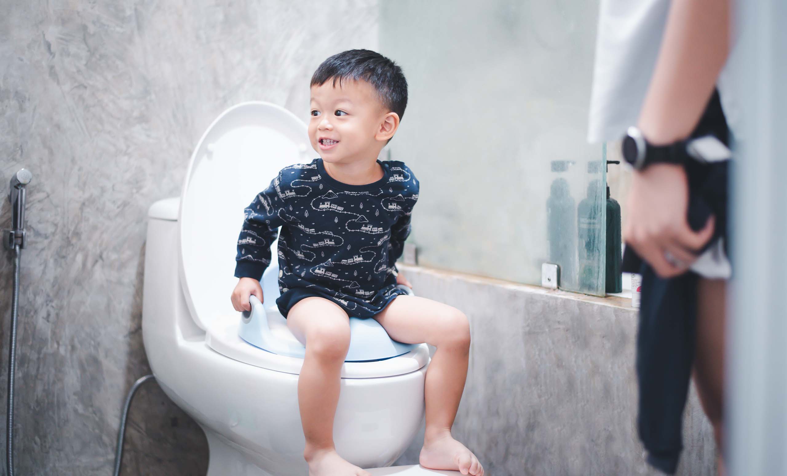 Young Asian toddler being potty trained by his parent.