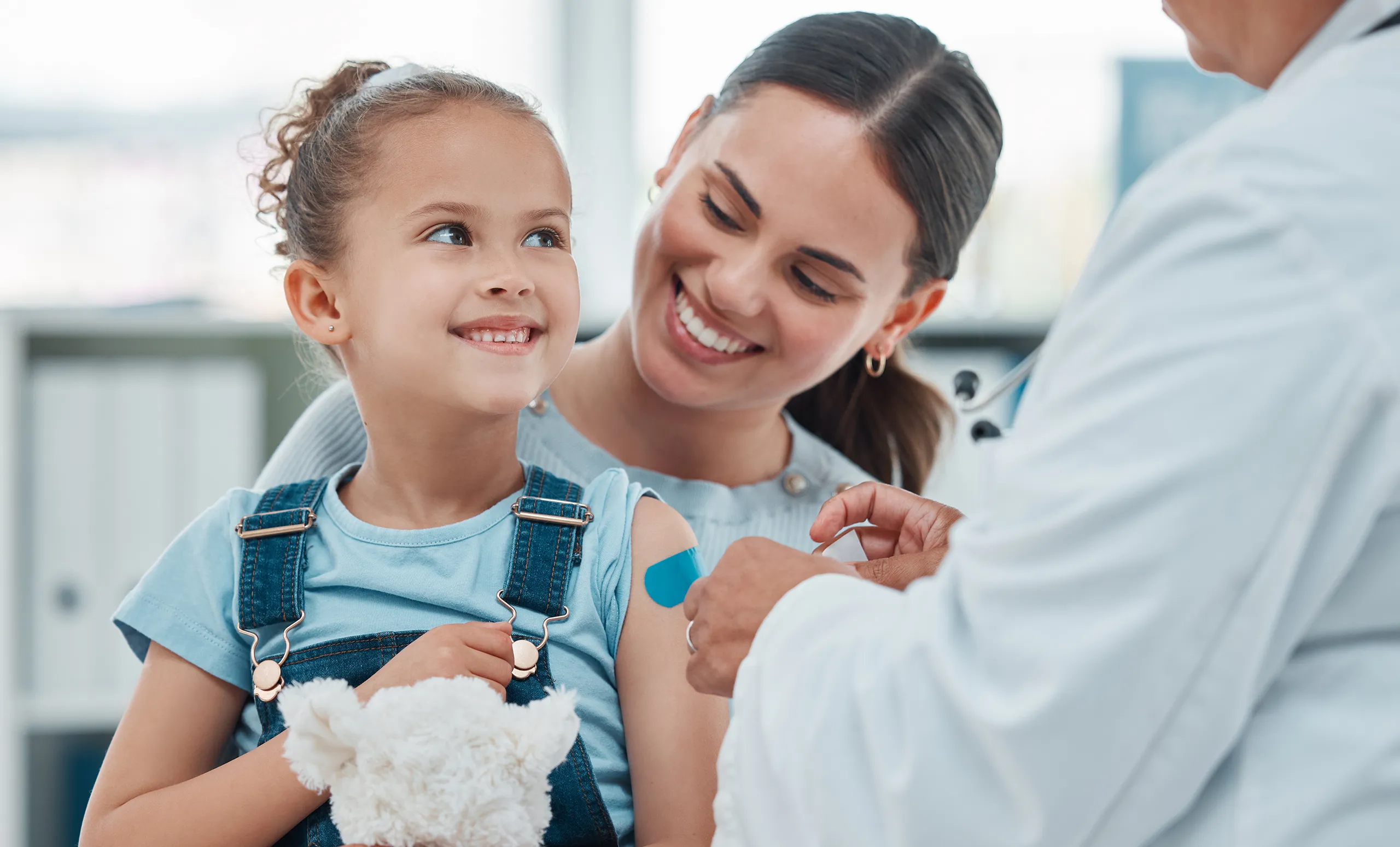 Smiling Hispanic mom holding her child as they get the flu vaccine at a doctors office.