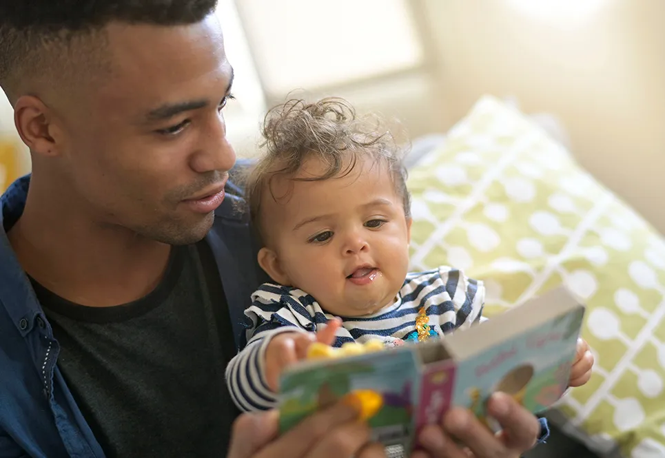 Young, black father reading books to his infant child.