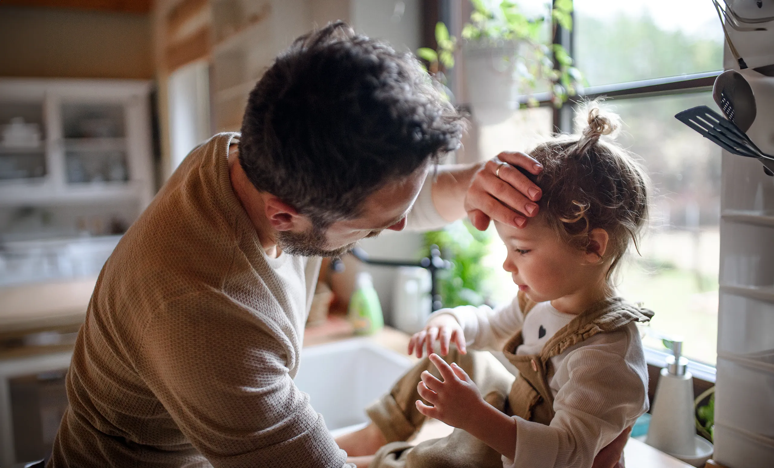 Father comforting a sick toddler in the kitchen of their home.