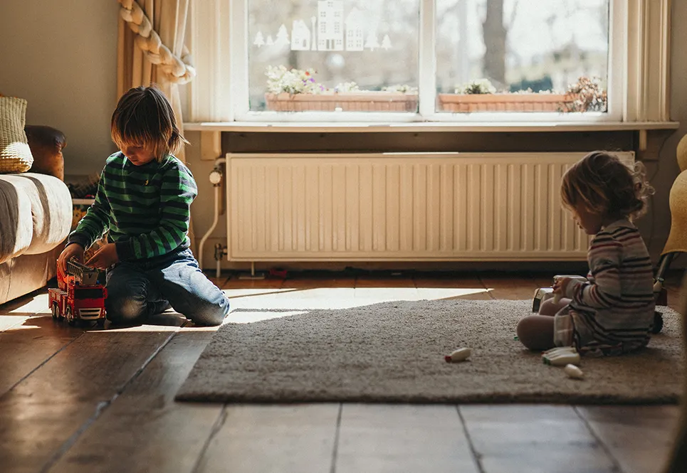  Two young siblings playing separated from each other in the living room.