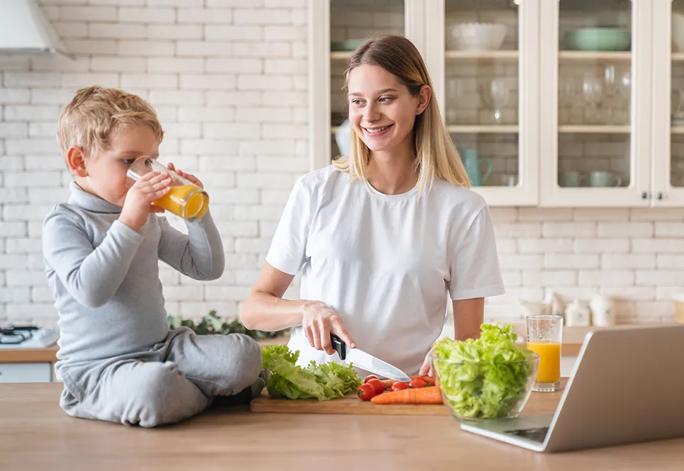 Mom making healthy food for a toddler, who is drinking orange juice.