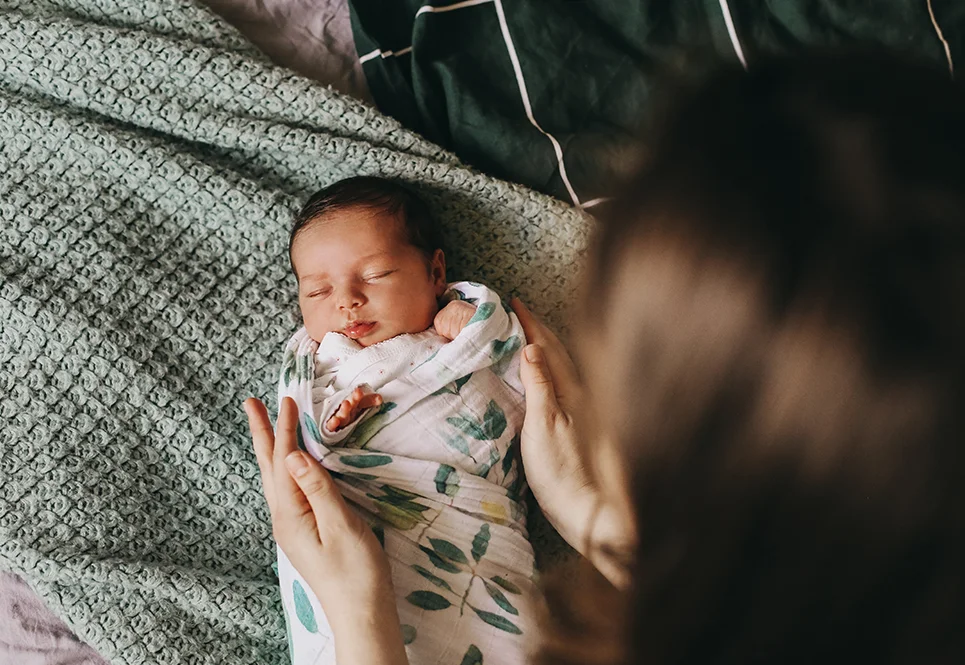 Sleeping baby being wrapped in a swaddle by mom.