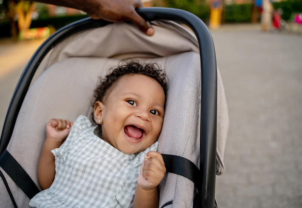 Smiling Black baby in a stroller on a walk with dad.