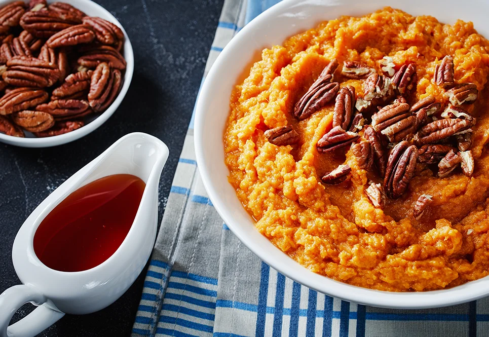 A bowl of mashed sweet potatoes topped with pecans