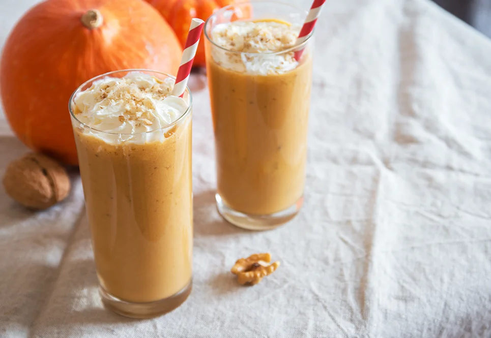 Two glasses filled with pumpkin pie smoothies and red and white striped straws