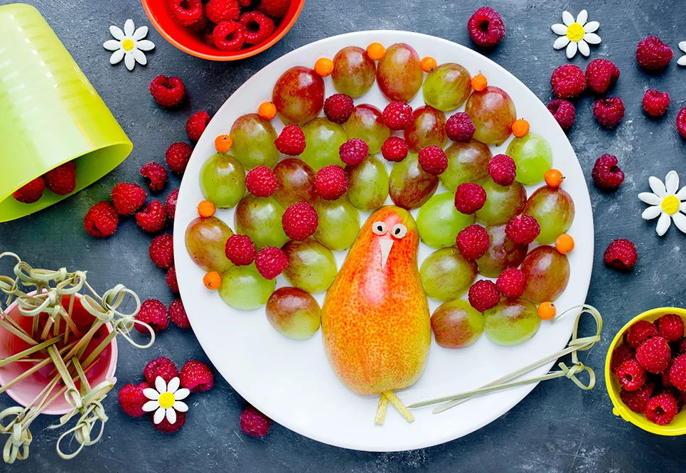 A plate filled with fruits shaped into a Thanksgiving turkey