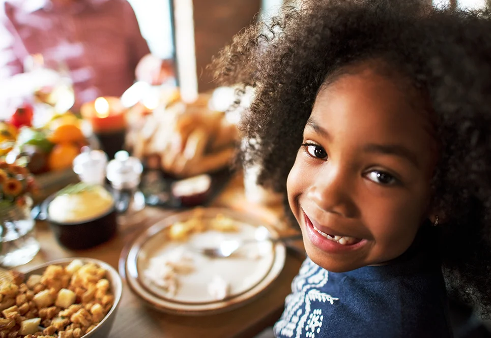 Young Black girl smiling at Thanksgiving dinner