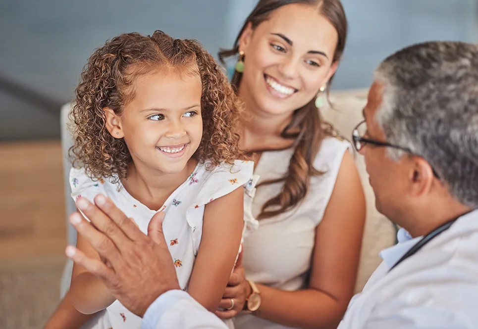 Ethnically ambiguous little girl on her mom’s lap high fiving her pediatrician