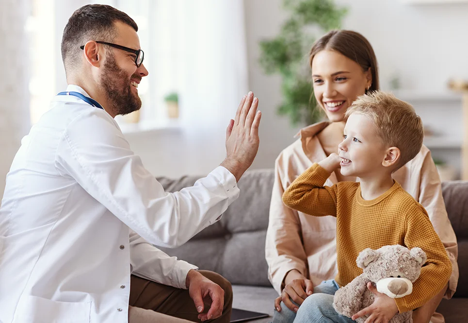 Little caucasian boy on his mom’s lap high fiving his pediatrician