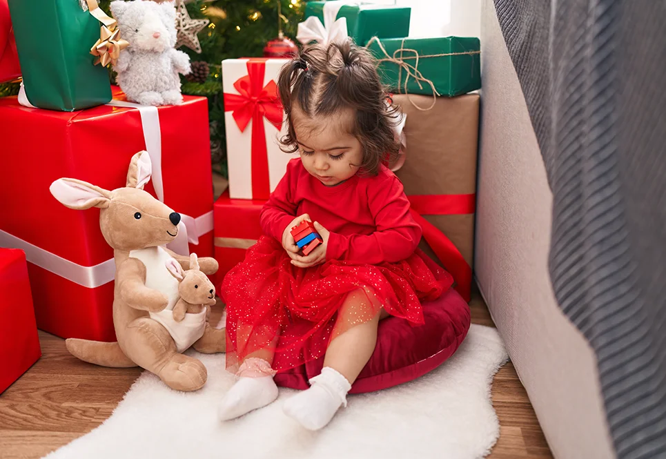 Hispanic toddler girl playing with a toy under a Christmas tree