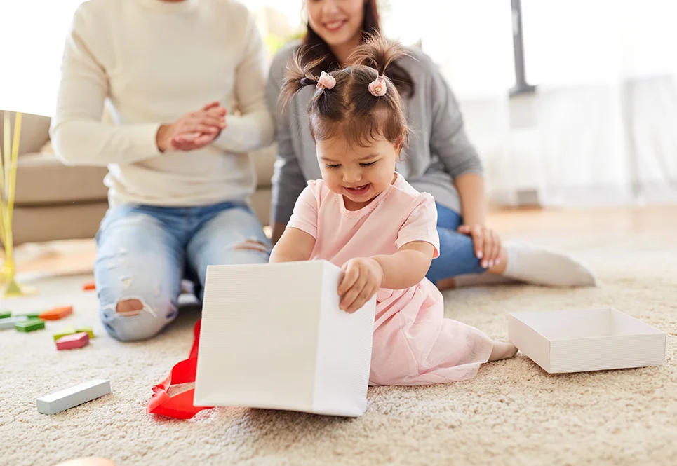 Ethnically ambiguous family watching their toddler girl open a gift