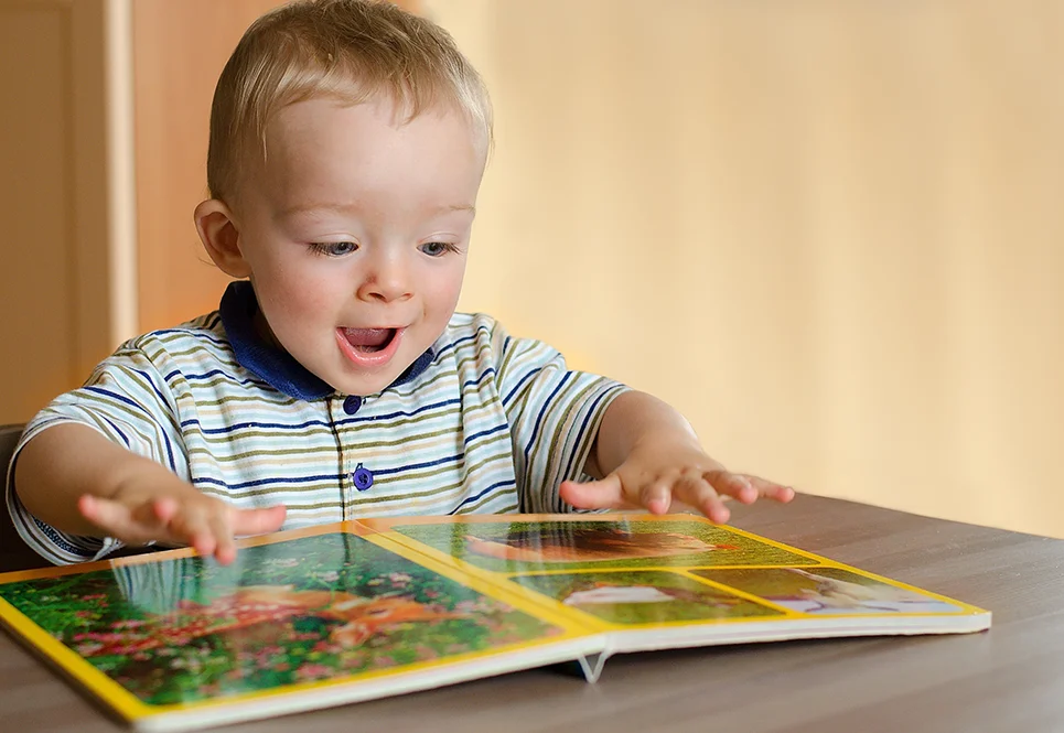 Excited caucasian toddler boy reading a picture book