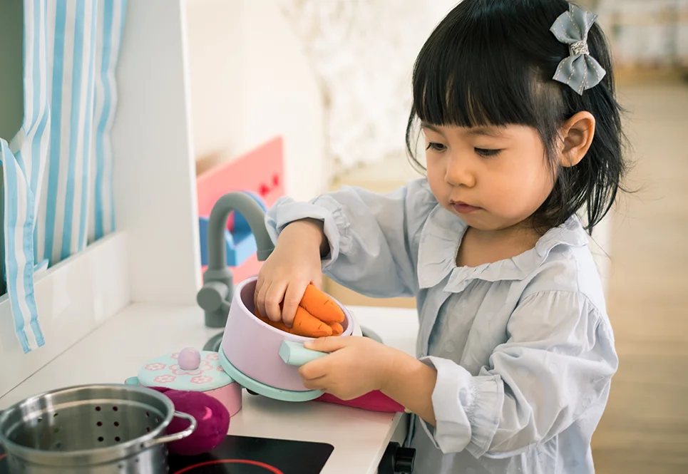 Asian toddler girl playing in a toy kitchen