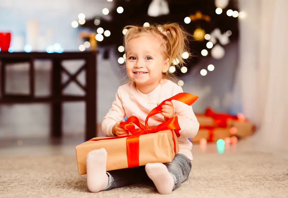 Blonde toddler girl opening a present at Christmas time