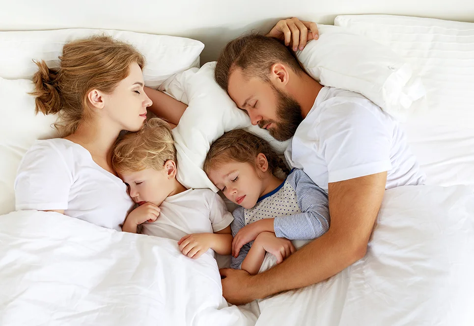 Family sleeping next to one another in bed. 