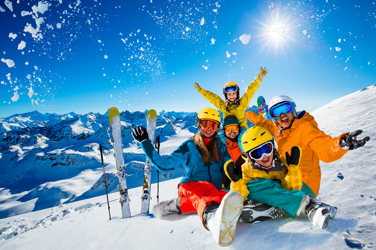 Excited family cheering on top of a mountain and all wearing skiing gear.