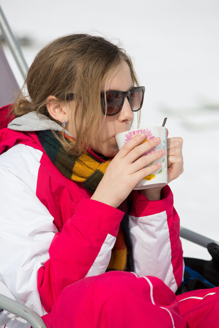 Closeup of younger teen girl drinking tea on a ski slope. 