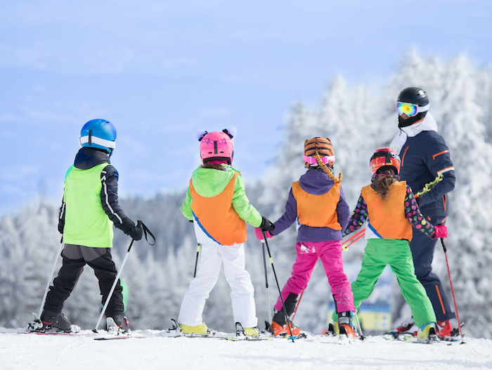 Young kids taking beginners ski lessons on a ski slope. 