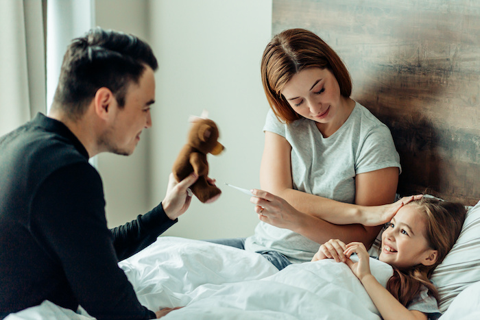 Young caucasian parents comforting their sick daughter in bed