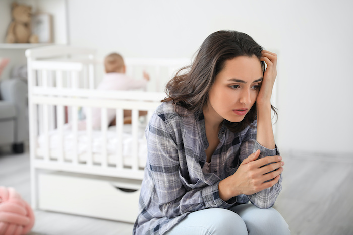 Young woman sitting at the edge of the bed, looking nervous. 