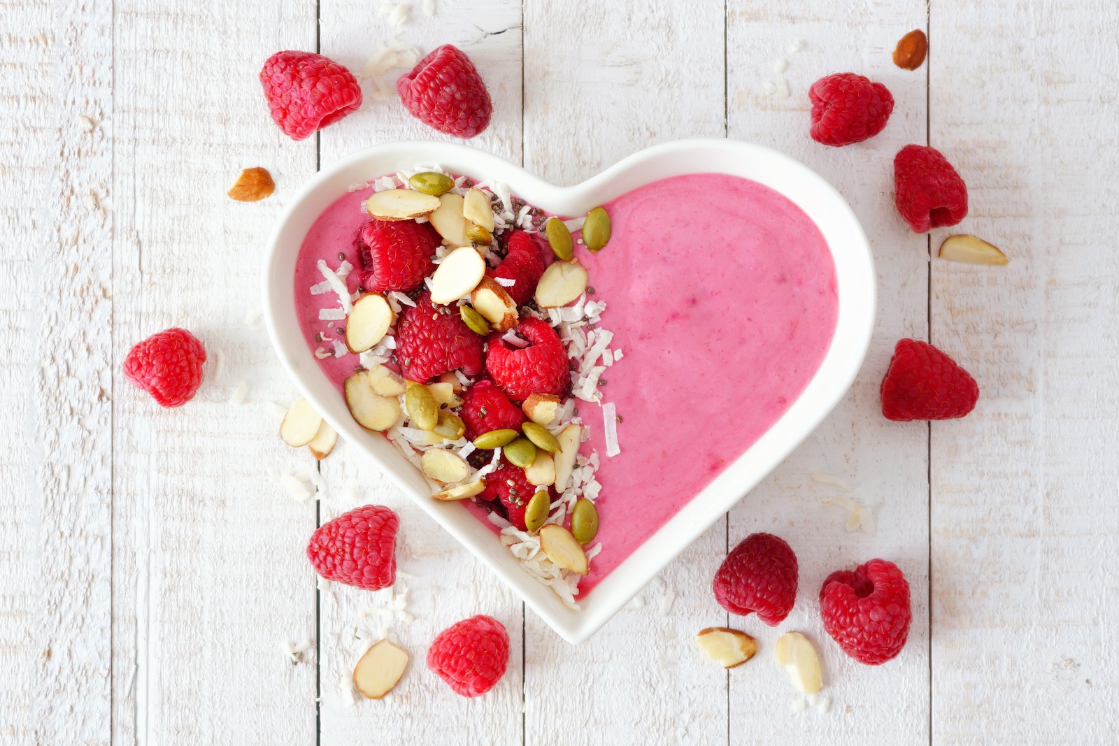 Heart-shaped bowl filled with a raspberry smoothie and other healthy toppings.