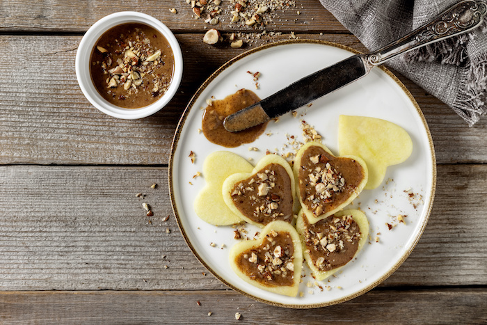 Apples cut into heart shapes with hazelnut butter spread on top of them. 