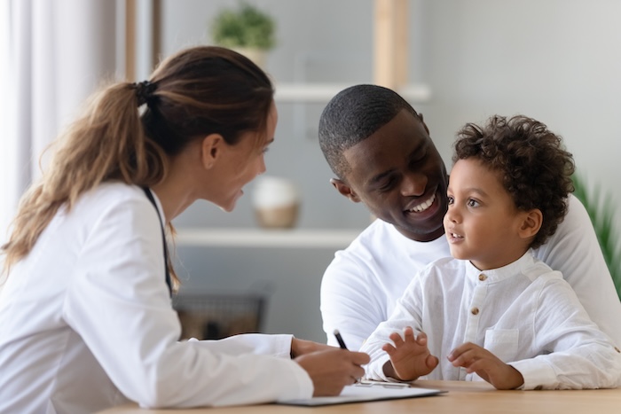 Mixed race little boy and Black father talking to a female pediatrician