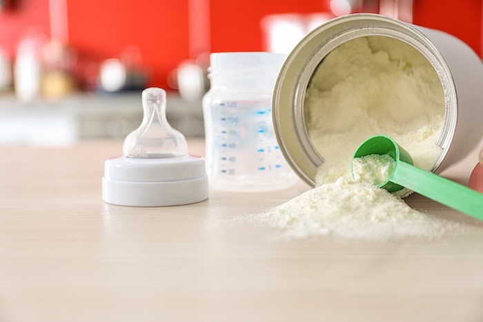 Spoonful of baby formula, with the can laying down on its side. 