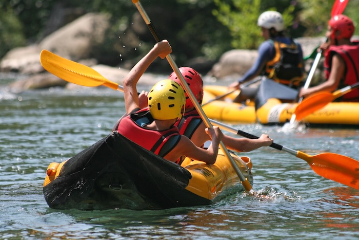 kids kayaking in a river, wearing protective gear. 