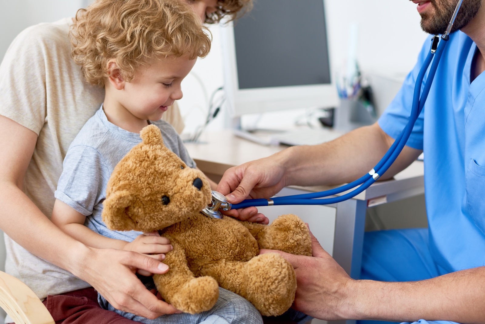 Pediatrician using his stethoscope on a young caucasian boy’s teddy bear