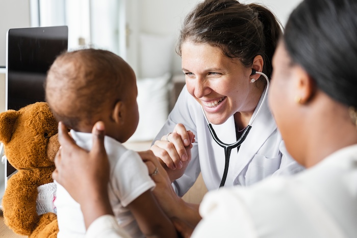 Caucasian female pediatrician smiling at with a Black baby patient