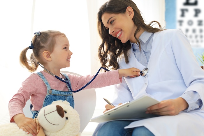 Little blonde girl playing with a stethoscope with her young female pediatrician