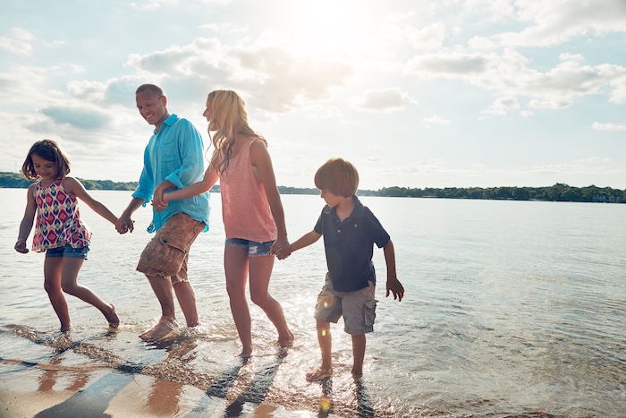 Family, playful and walking in beach or holding hands and travel for summer, holiday and nature of California. Parents, kids and adventure in tropical sea and man with woman, water and children.