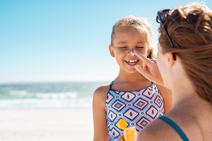 Mom putting sunscreen on her young daughter’s nose. 