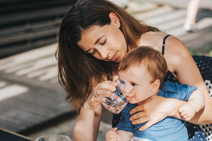 Mom giving water to a young boy that is overheated. 