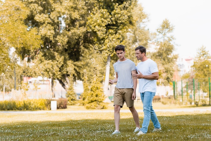 Father in a white t shirt, talking to his teen son on a walk. 