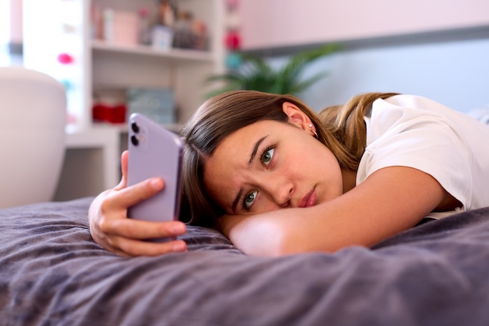Teen girl looking depressed as she scrolls on her smartphone. 