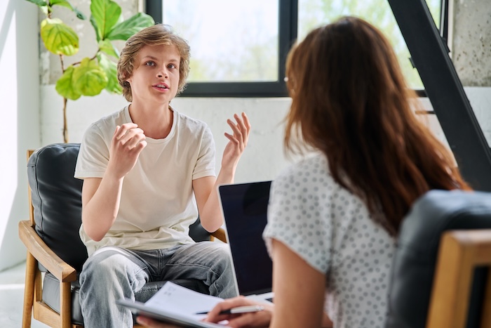 Young blonde teen boy talking to a child psychologist in their office. 