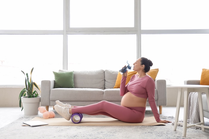 Pregnant woman drinking water on a yoga mat. 
