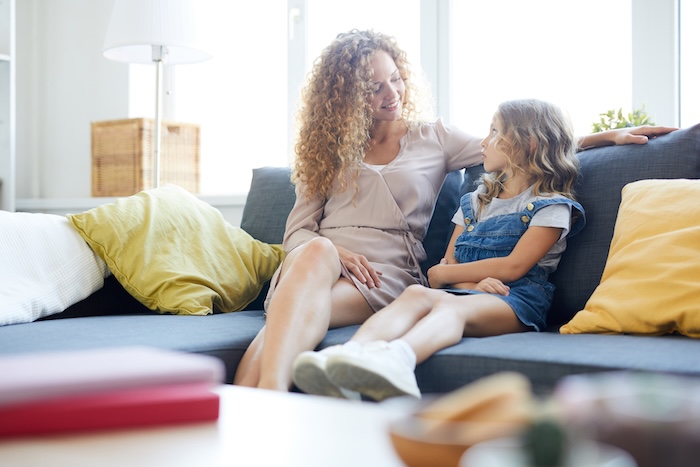 Blonde-haired mother talking to her child on the couch. 