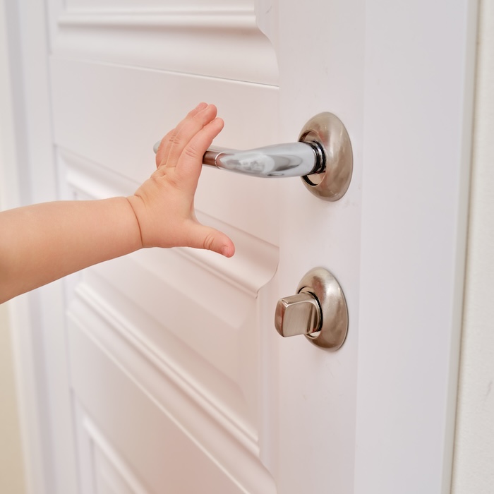 Closeup of child’s hand reaching for a doorknob. 