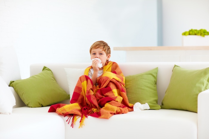 Little boy sitting on a couch, sick with a cold. 