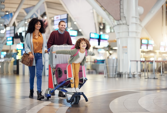 Airport, family and child excited for flight with suitcase trolley on holiday, vacation or immigration journey and travel. Luggage of mother, father or diversity parents with girl kid flying in lobby.