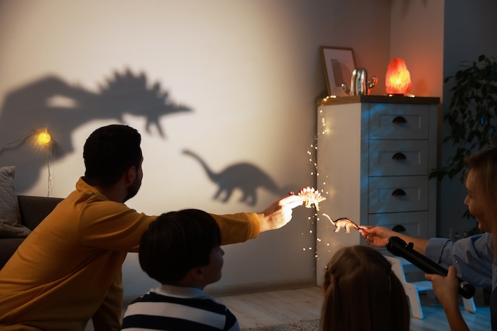 Mixed race family putting on a shadow puppet show with toy dinosaurs