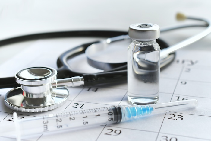 Closeup of a vaccine, stethoscope and calendar.