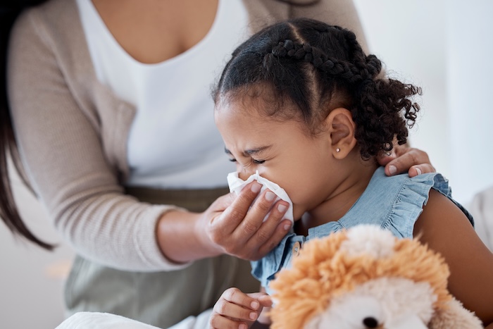 Black mother helping young daughter blow her nose.