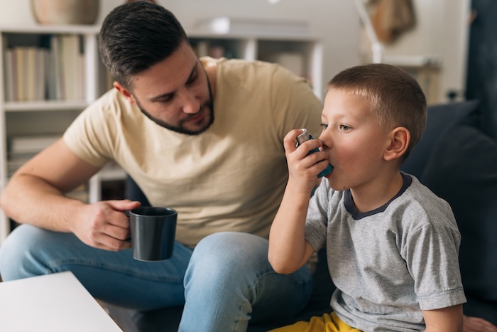 Father of an asthmatic child helping him use an inhaler.