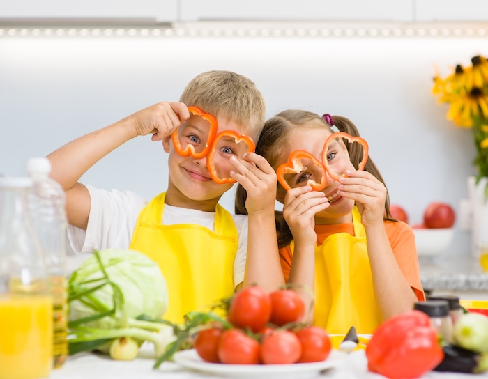 Two young children making faces while holding bell pepper slices.